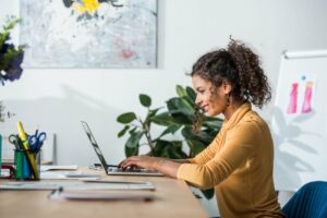 Black woman side profile sitting at desk with hands on laptop keyboard